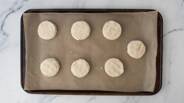 A large, parchment-lined baking sheet with raw biscuits