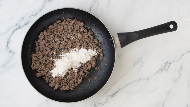 Cooked breakfast sausage sprinkled with flour in a large skillet