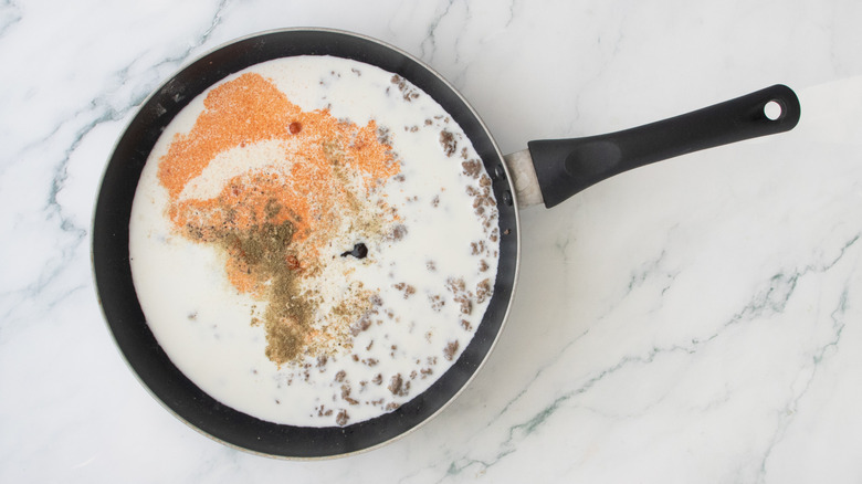 A large skillet filled with cooked sausage, milk, and seasonings