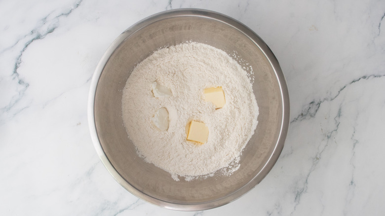 A large metal bowl filled with dry baking ingredients and pats of butter and shortening