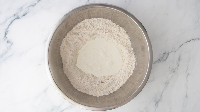 A large metal bowl with flour and a well in the center filled with buttermilk