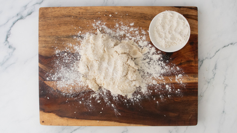 A wood cutting board with flour-dusted dough