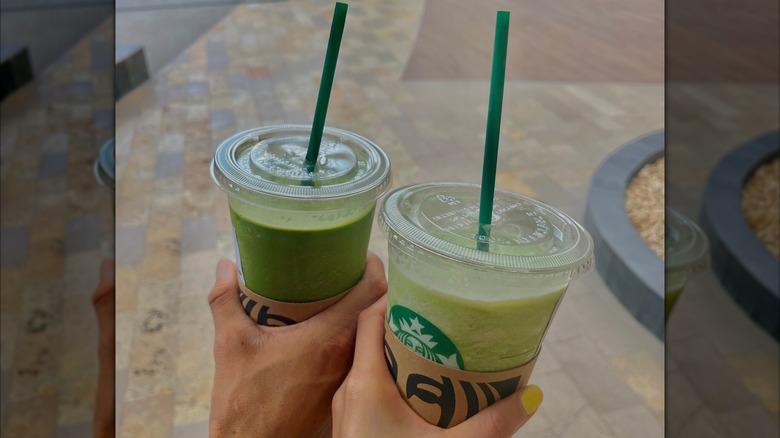 hands hold two starbucks green drinks