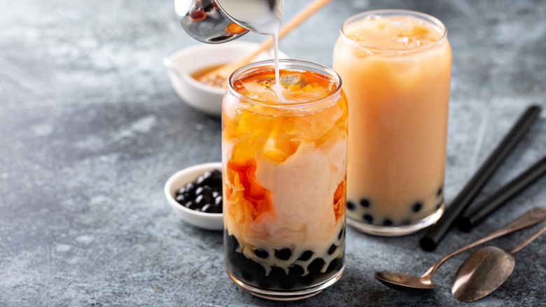 Boba tea with tapioca pearls and cream being poured in