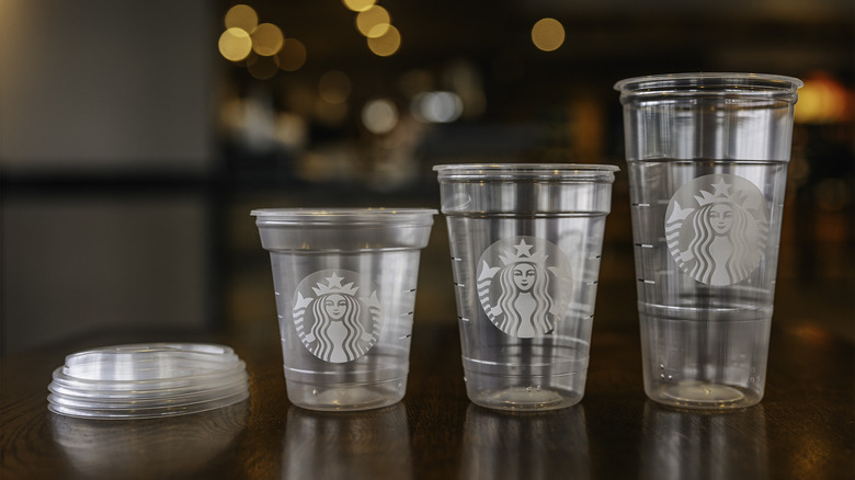 Three Starbucks cold cups with lids on the side on wood table