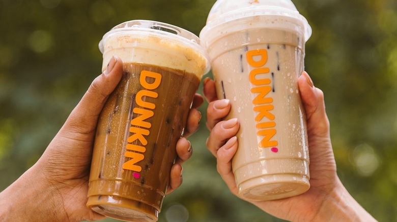 Closeup hands holding Dunkin Pumpkin Cream Cold Brew and Pumpkin Spice Signature Latte