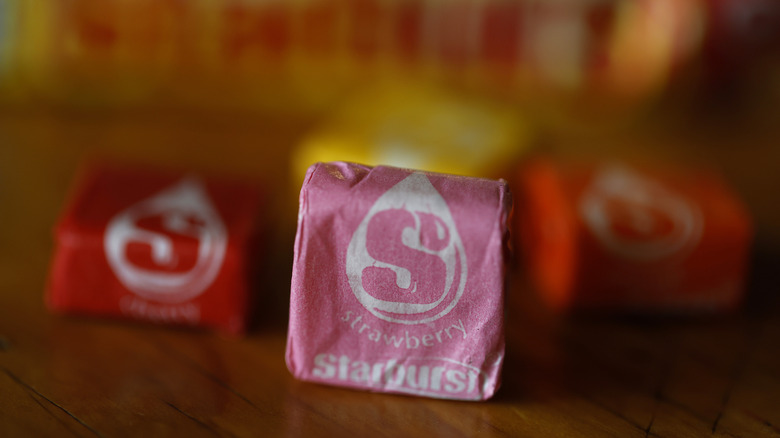 Closeup of pink Starburst candy in wrapper, other candies in background.