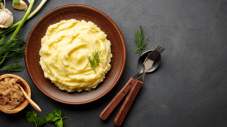 Mashed potatoes in wood bowl on dark background with fork and spoon