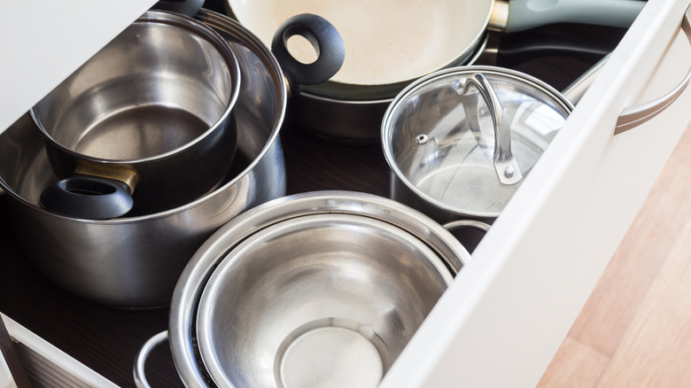 Open drawer of cabinet with metal pots and pans.
