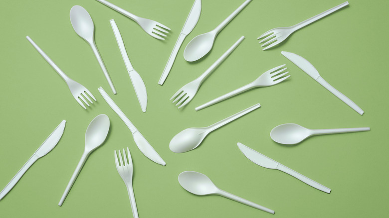 Scattered white plastic silverware on green background, overhead view.