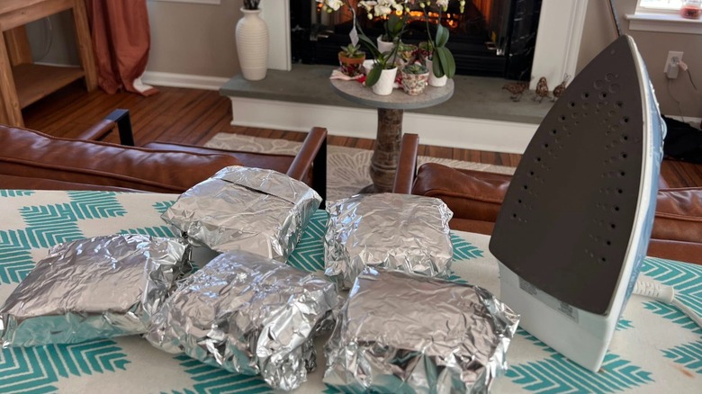 Foiled grilled cheese sandwiches and an iron on a table