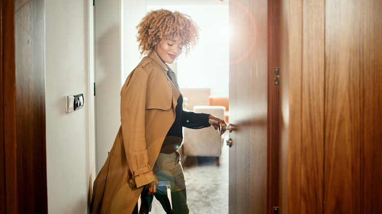 Woman entering hotel room with rolling suitcase.