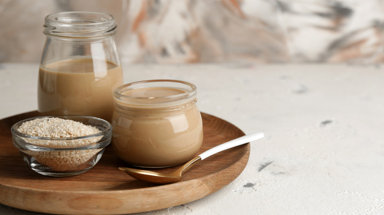 Jars of tahini sauce besides a container of sesame seeds.