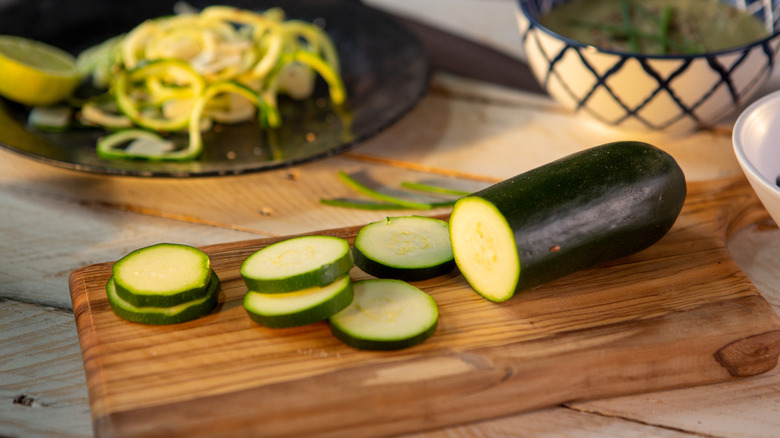 Zucchini slices and half a zucchini on a wooden cutting board