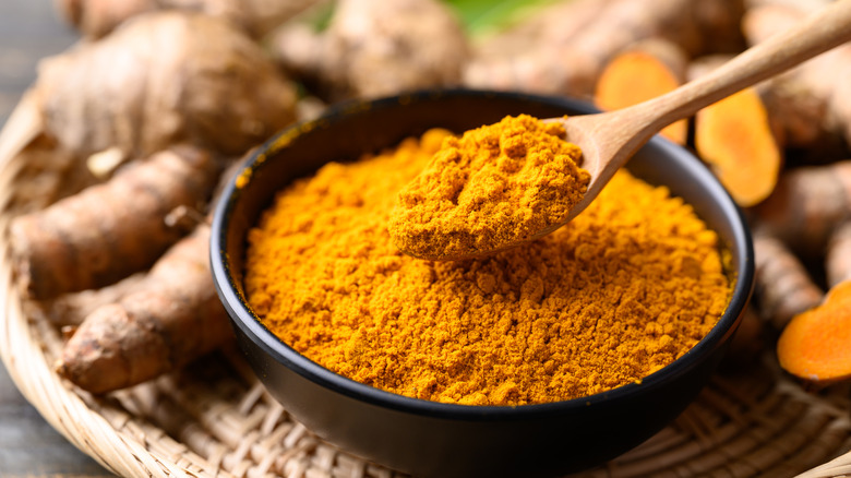 A small bowl of turmeric powder with a wooden spoon scooping some out