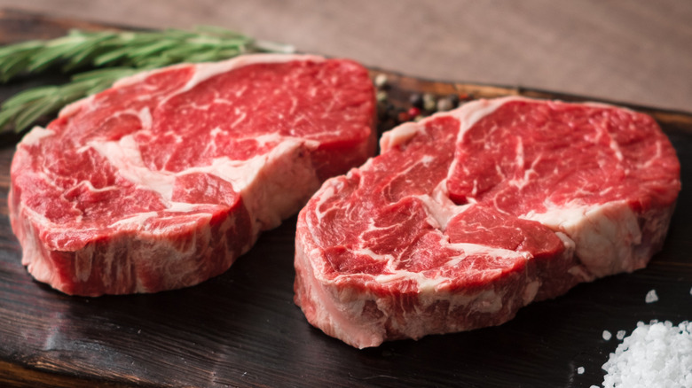 Two slices of rib eye steak on a wooden board