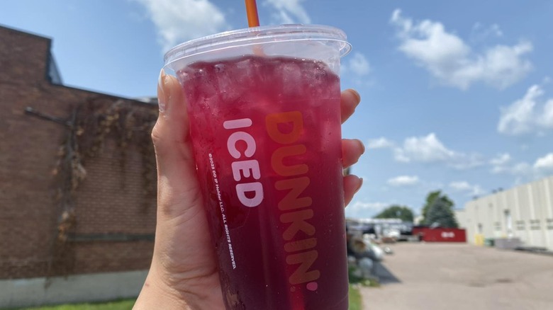 Hand holding a plastic cup of Dunkin' Blueberry Breeze Refresher outside