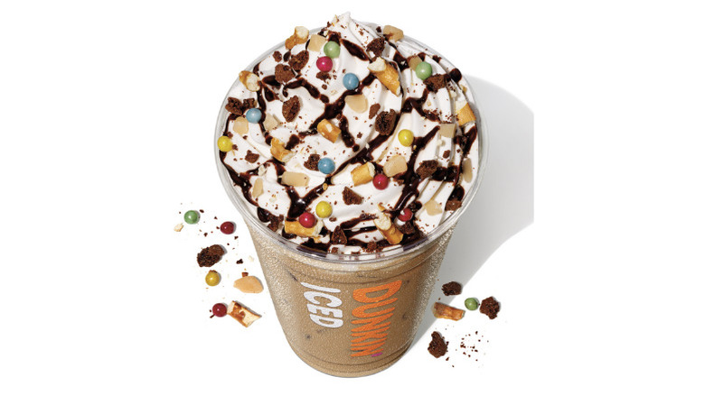 Angled image of plastic cup with Candy Bar Latte topped with whipped cream, drizzles, candy, and pretzels