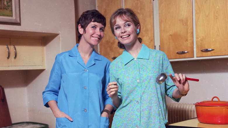 Two women in 1960s dresses standing in kitchen smiling.