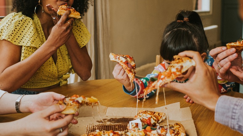 big group eats takeout pizza around a table