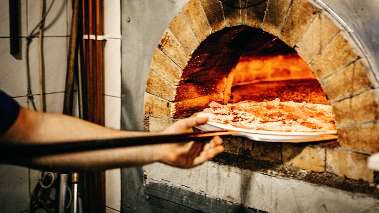 an arm puts a pizza into a brick oven