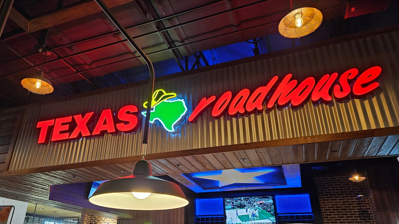 A neon Texas Roadhouse sign located inside its restaurant, above the dining area