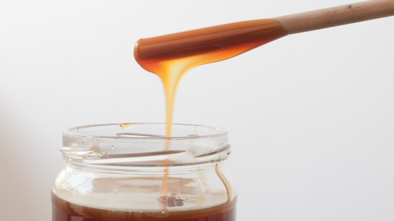 A wooden stick dripping barley malt syrup back into a jar