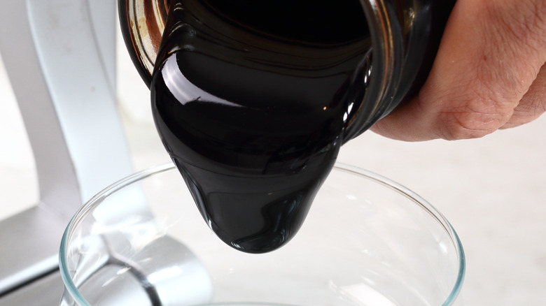 Blackstrap molasses pouring from a jar into a clear glass bowl