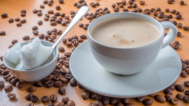 A cup of coffee next to a spoonful of coconut oil