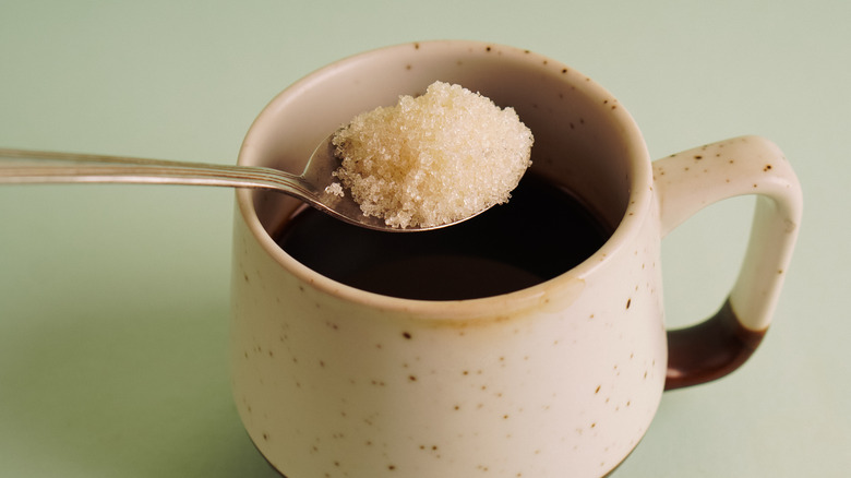 Close up of a spoonful of sugar over a cup of coffee
