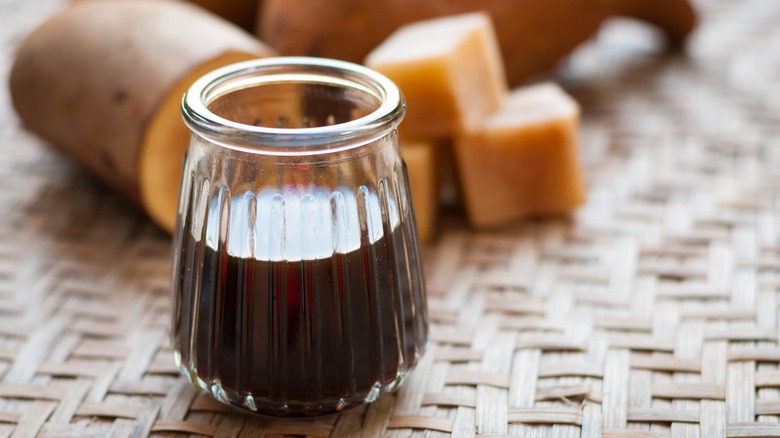 Yacon syrup in a glass container with fresh yacon roots in the background