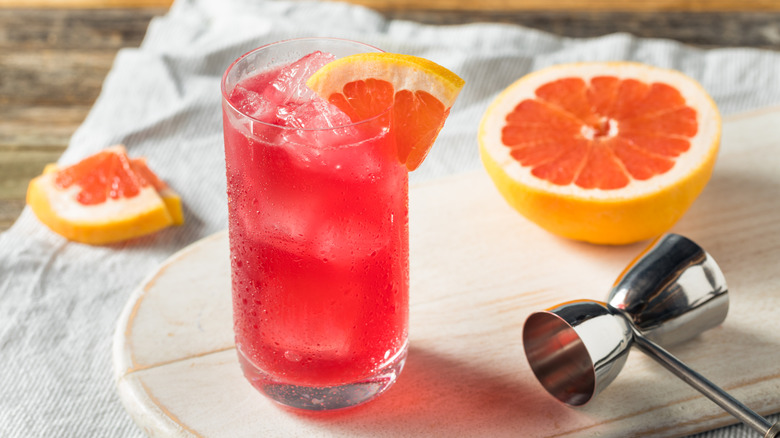 A close-up of a sea breeze cocktail in a glass with a wedge of grapefruit in the rim, along with more grapefruit wedges to the left and a half a grapefruit to the right