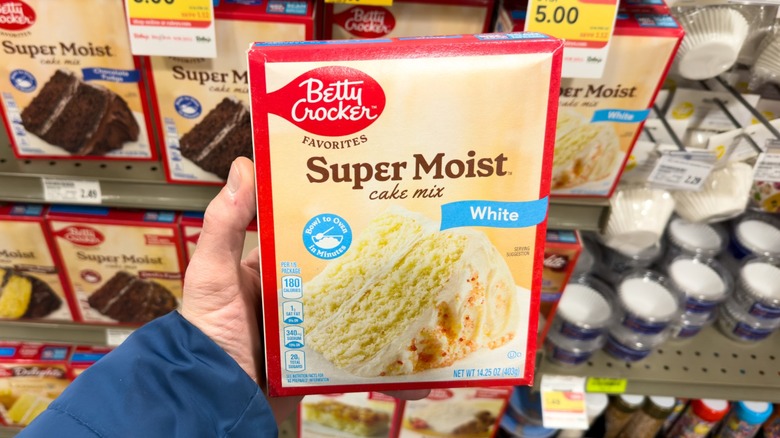a hand holds a box of white cake mix