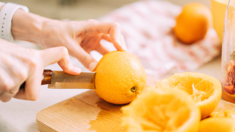 A close-up of someone cutting oranges to make juice, with a few squeezed oranges to the side