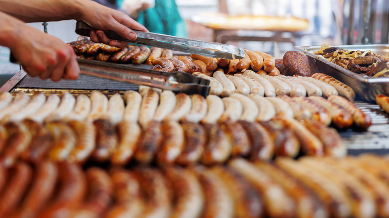 hands grilling an assortment of sausages using tongs