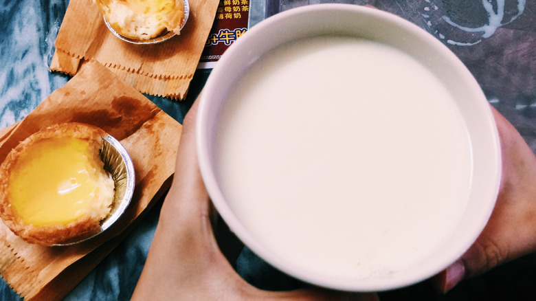 Hands holding white bowl of ginger milk pudding with tarts on the side.
