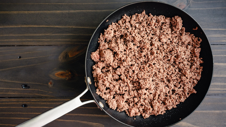 Cooked ground beef in pan on wood surface.