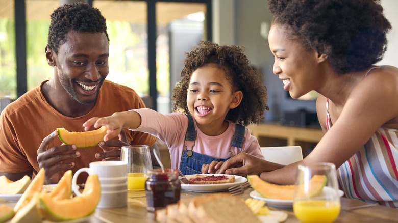 A happy family of three eating breakfast at the dining room table