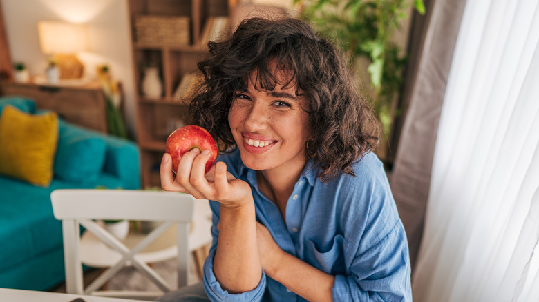 Woman sits at table, smiling while holding an apple.