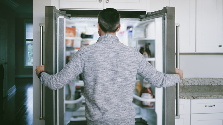 Man standing in front of fridge, holding both doors open.