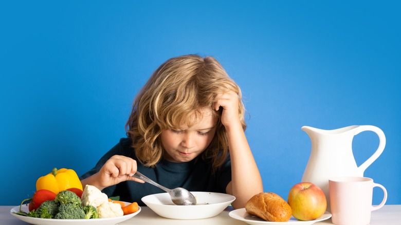a child frowns at a bowl of soup