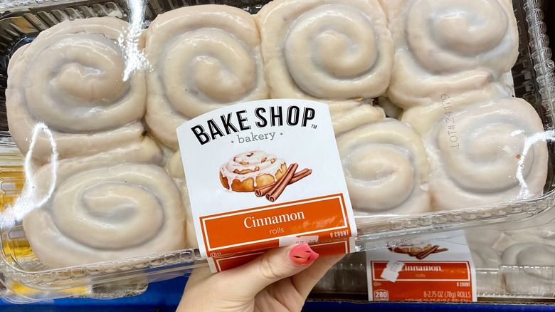 Hand holds up Aldi Bake Shop Cinnamon Rolls against grocery display case