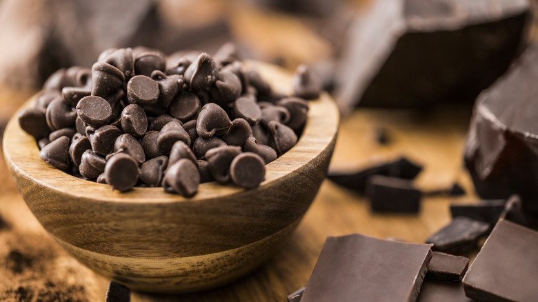 wooden bowl of chocolate chips surrounded by chocolate chunks on a wooden table