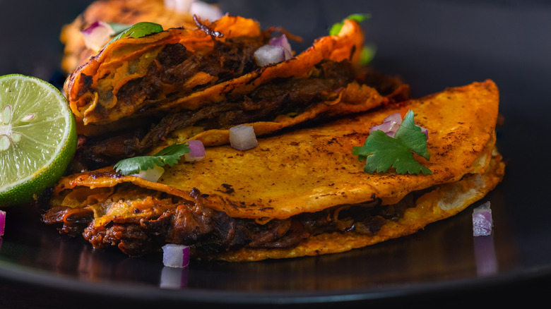 Three birria tacos stacked on top of each other on a black plate