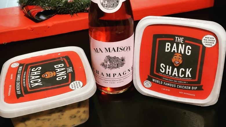 Bottle of champagne flanked by two packages of The Bang Shack chicken dip