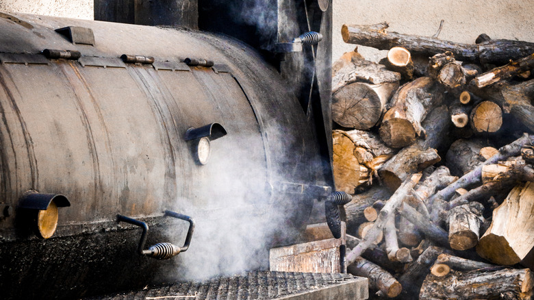 Old smoker grill in use with adjacent woodpile