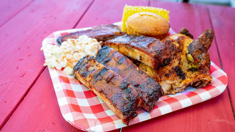 Pork spare rib dinner with sides on red and white disposable plate.