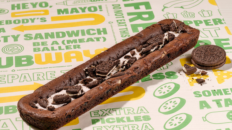 A Subway Oreo footlong cookie on branded paper, next to a full Oreo cookie and a few crumbs