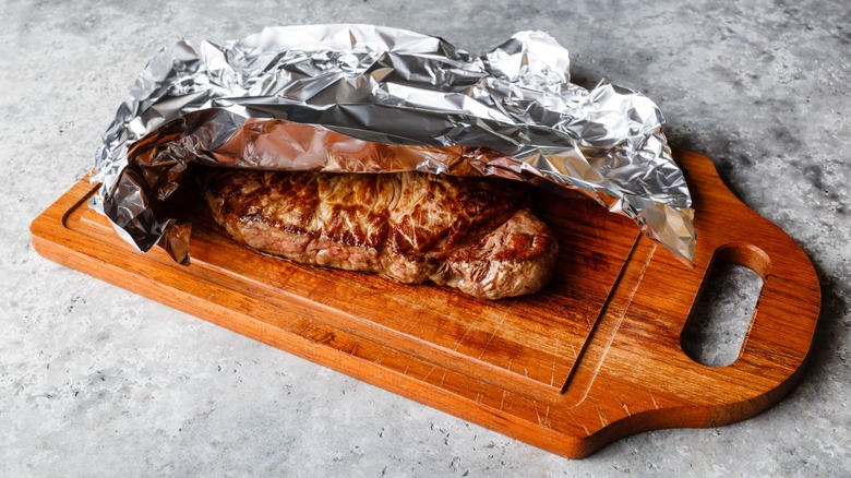 resting beef on a cutting board with a foil tent