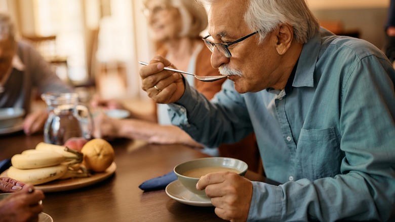 older man eats soup at table with friends